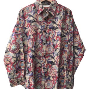 May include: Button-down shirt with a colorful floral pattern in red, blue, and beige. The long-sleeved shirt is made of a lightweight fabric and hangs on a wooden hanger. The shirt features a classic collar and buttoned cuffs.