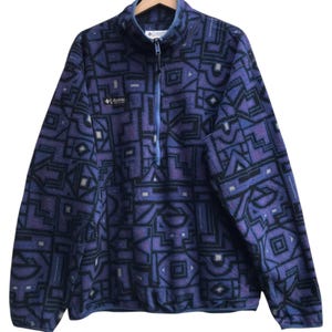 May include: A vintage Columbia fleece jacket in a striking geometric pattern. The jacket features a half-zip closure, a stand-up collar, and the Columbia logo. The primary colors are purple, black, and gray, creating a bold and retro aesthetic.