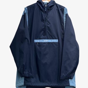 Peut inclure: Un coupe-vent Nike à enfiler bleu marine et bleu clair doté d'une capuche avec cordons de serrage, d'une fermeture éclair à mi-hauteur, de manches longues à poignets élastiques et d'une poche frontale zippée avec le logo Nike en blanc.