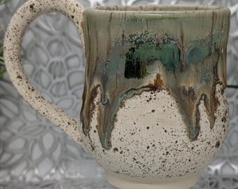 Hand thrown and trimmed 15 oz footed porcelain coffee mug in green metallic in places brown and brown speckled cream glaze