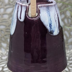 May include: A purple ceramic yarn bowl with white and blue glaze accents. The bowl has a hole in the top for a yarn needle.