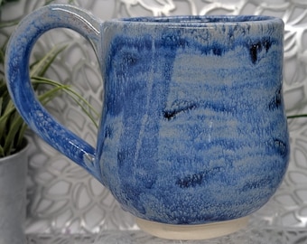 Hand thrown and trimmed 17 oz footed short porcelain coffee mug in variegated dark blue glaze.