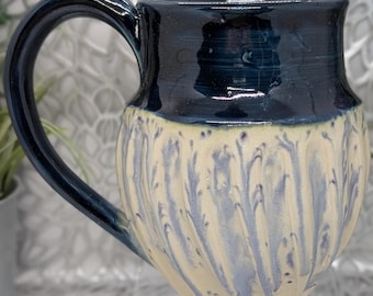 Hand thrown and carved 26 oz tall fluted porcelain mug in dark blue celadon and cream with melting blue specks.
