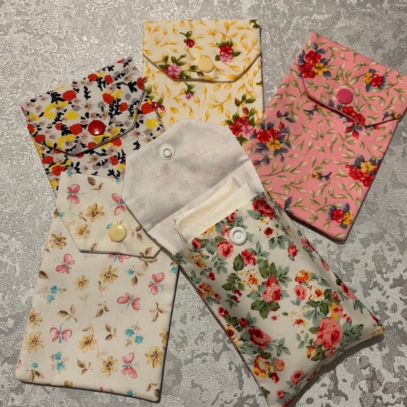 May include: Five fabric pouches with floral patterns. The pouches have a flap with a button closure. The pouches are in various colours, including pink, yellow, and white.