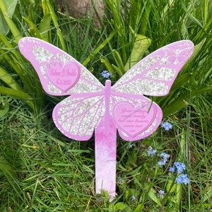 Peut inclure: Piquet de jardin en forme de papillon rose avec des accents de paillettes. Le piquet a une plaque en forme de cœur avec le texte "Vos ailes étaient prêtes mais nos cœurs ne l'étaient pas". Une deuxième plaque en forme de cœur porte le texte "Kalina L Dodds 6-3-2023".