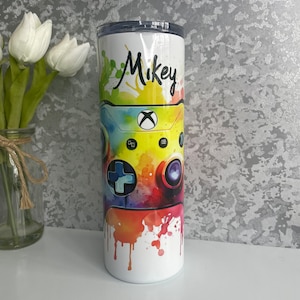 Könnte beinhalten: Ein weißer Becher mit einem farbenfrohen Aquarelldesign eines Videospiel-Controllers. Der Name "Mikey" ist in schwarzer Kursivschrift auf dem Becher geschrieben.