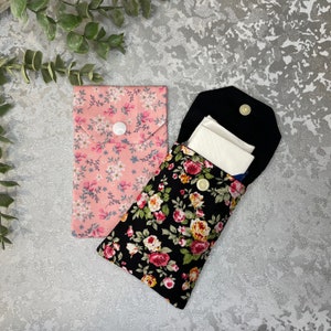 Peut inclure: Deux pochettes en tissu avec des motifs floraux. Une pochette est rose avec des fleurs blanches et l'autre est noire avec des fleurs colorées. Les deux pochettes ont une fermeture à bouton.
