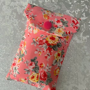 May include: A pink floral fabric pouch with a flap closure and a pink button. The pouch is ideal for storing small items such as jewellery, coins, or keys.