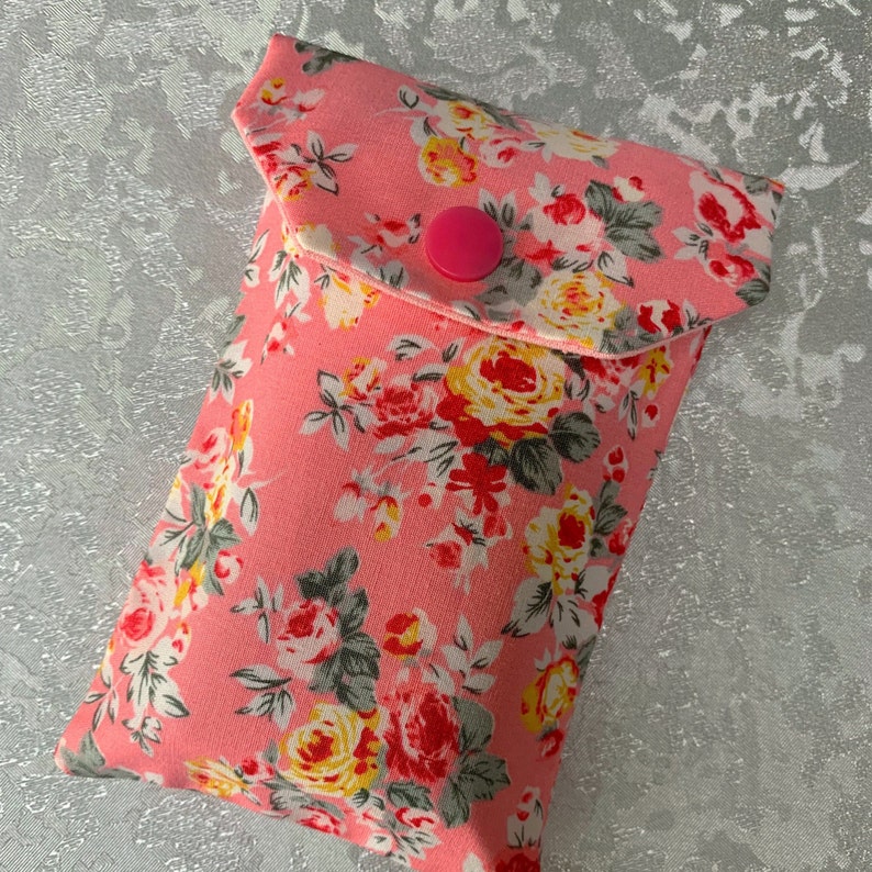 May include: A pink floral fabric pouch with a flap closure and a pink button. The pouch is ideal for storing small items such as jewellery, coins, or keys.
