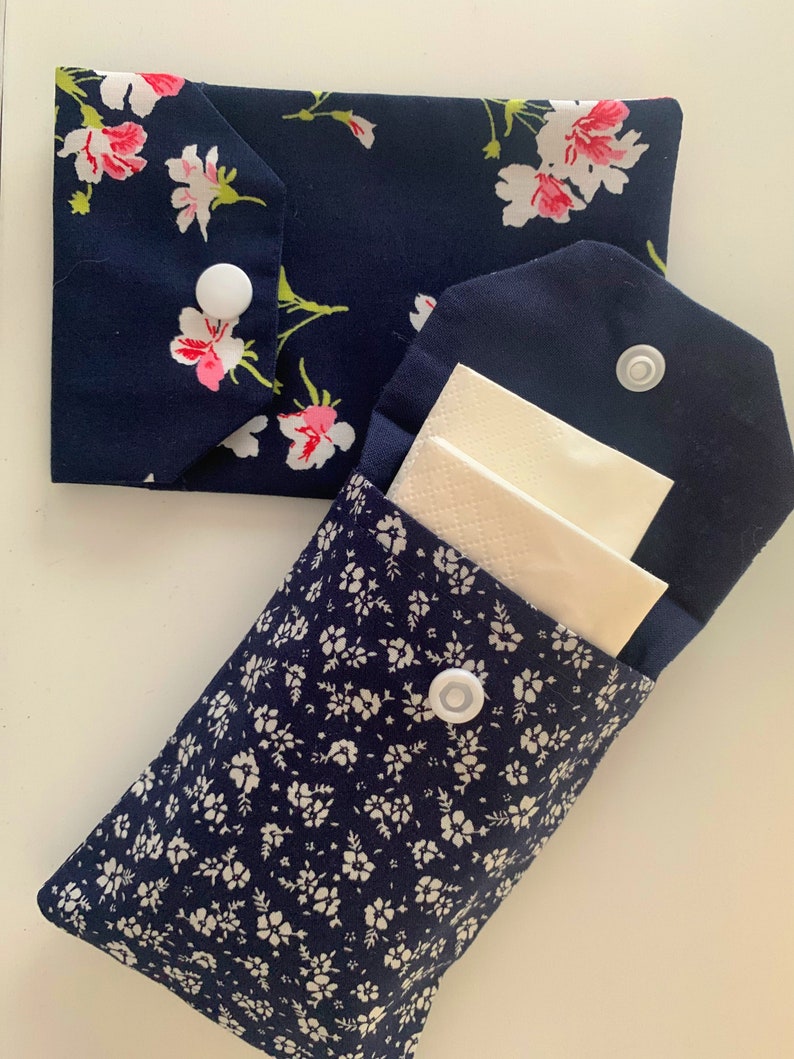 May include: Two fabric pouches with floral patterns. The smaller pouch is navy blue with white and pink flowers. The larger pouch is navy blue with a white floral pattern. Both pouches have white buttons.