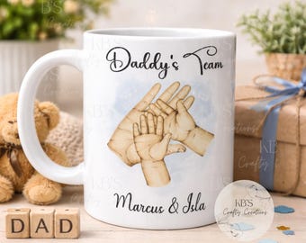 May include: White ceramic mug with the text "Daddy's Team" and the names "Marcus & Isla". The mug features a watercolor illustration of hands, with a large hand holding two smaller hands. A perfect gift for Father's Day.