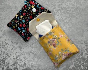 May include: Two fabric pouches with floral patterns. The smaller pouch is black with red, pink, and blue flowers. The larger pouch is yellow with pink, blue, and white flowers. Both pouches have white buttons and are open to reveal a white tissue.