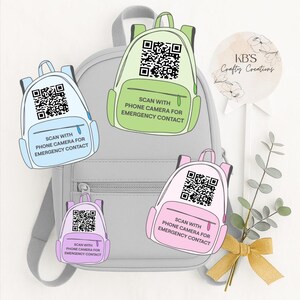 Könnte beinhalten: Ein grauer Rucksack mit vier bunten QR-Code-Anhängern in Rucksackform. Jeder Anhänger hat eine andere Farbe: hellblau, grün, rosa und lila. Der Text auf jedem Anhänger lautet: "MIT DER HANDYKAMERA FÜR NOTFALLKONTAKT SCANNEN."