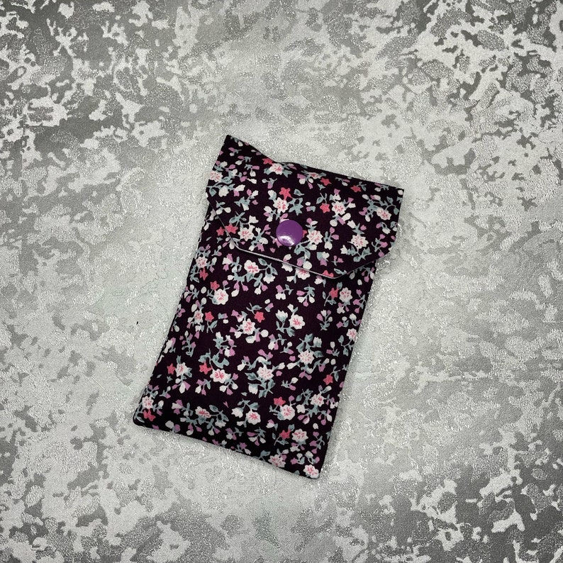 May include: A small purple fabric pouch with a floral print. The pouch has a flap with a purple button closure.