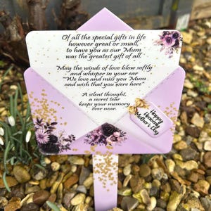 Pode incluir: Estaca de jardim memorial floral roxa e dourada com o texto "De todos os presentes especiais da vida, por maiores ou menores que sejam, ter você como nossa Mãe foi o maior presente de todos. Que os ventos de amor soprem suavemente e sussurrem em seu ouvido "Nós amamos e sentimos sua falta Mãe e desejamos que você estivesse aqui" Um pensamento silencioso, uma lágrima secreta mantém sua memória para sempre. Feliz Dia das Mães Celestial"