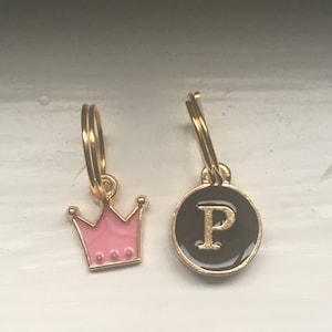 May include: Two gold-colored charms, one shaped like a pink crown and the other a black circle with a gold letter "P" in the center.