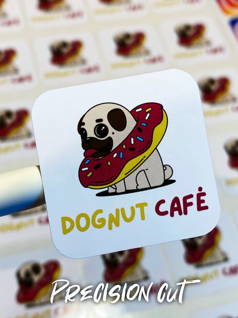 Pu&ograve; includere: Un adesivo bianco con un carlino dei cartoni animati che indossa una ciambella rossa e gialla. Il testo "DOGNUT CAFE" &egrave; scritto in lettere gialle e rosse.