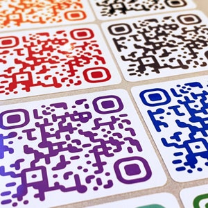 May include: A selection of QR code stickers in a range of colours, including orange, red, black, purple, and blue. Each sticker features a white background and a unique pattern. The stickers are arranged in a grid formation.