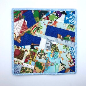 May include: A blue and white patchwork quilt square with a Christmas theme. The square is made up of various fabrics with different patterns, including dogs, reindeer, and snowflakes. The square is edged with a light blue fabric.