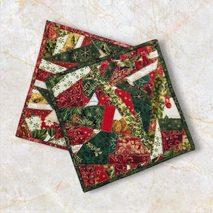 May include: Two green, red and gold Christmas-themed pot holders with a patchwork design. The pot holders feature the words "Merry Christmas" and "Joyeux Noel".