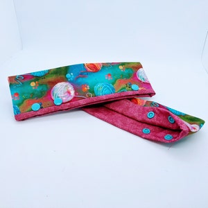 May include: A pair of fabric headbands with a colorful yarn ball print and a solid burgundy color. The headbands have turquoise snap buttons.