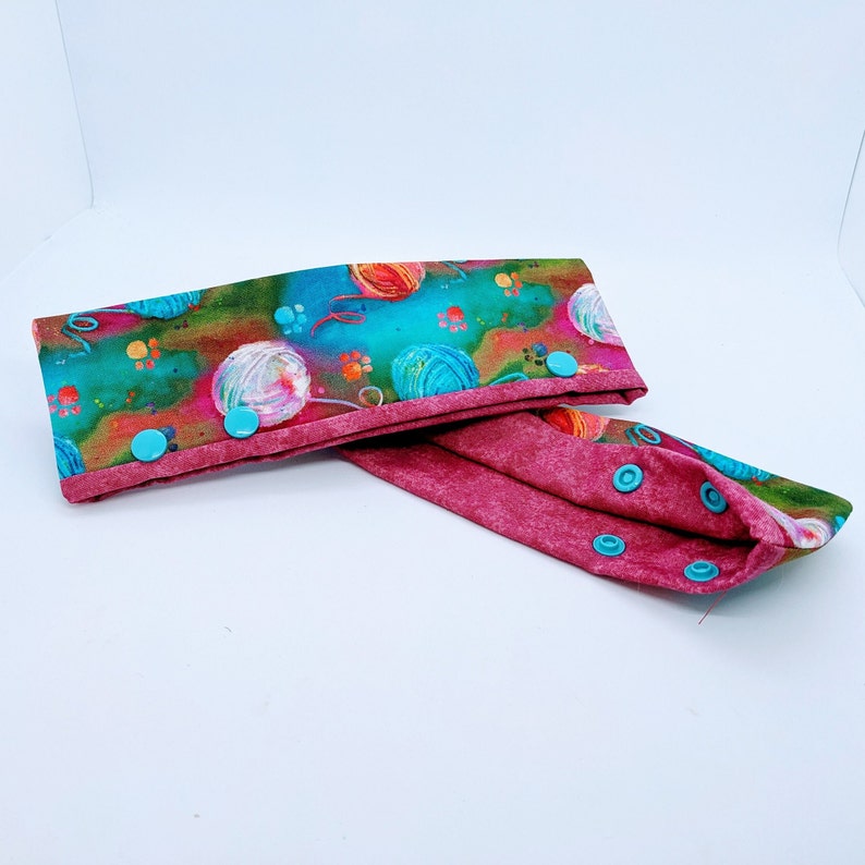 May include: A pair of fabric headbands with a colorful yarn ball print and a solid burgundy color. The headbands have turquoise snap buttons.