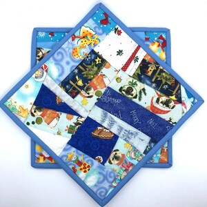 May include: Two blue and white patchwork pot holders with a Christmas theme. The pot holders feature a variety of holiday designs, including pugs, snowflakes, and the words "Merry Christmas" and "Noel".