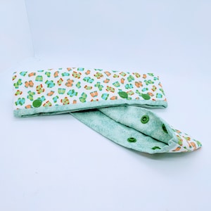 May include: A white fabric headband with a green and orange print of socks. The headband has green snap buttons and is folded in half.