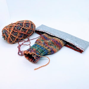 May include: A colorful knitted sock with a gray fabric band and a ball of yarn in orange, red, and brown.