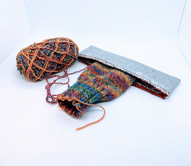 May include: A colorful knitted sock with a gray fabric band and a ball of yarn in orange, red, and brown.