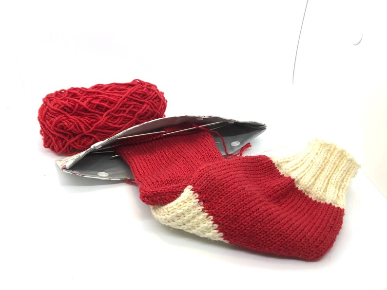 May include: A red and white striped knitted sock with a ball of red yarn and knitting needles.