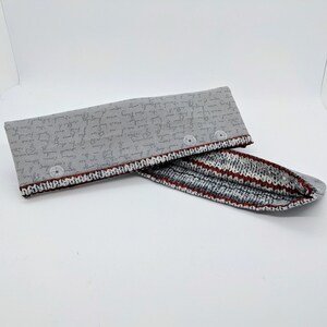 May include: A gray fabric pouch with a red and white striped lining. The pouch has a zipper closure and is decorated with a pattern of handwritten text.