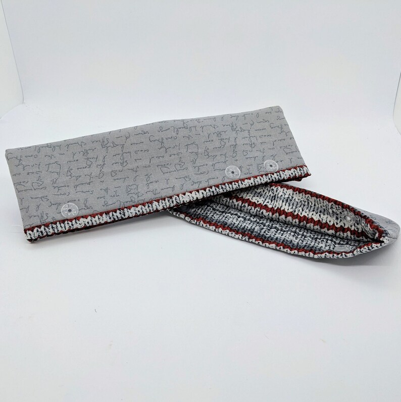 May include: A gray fabric pouch with a red and white striped lining. The pouch has a zipper closure and is decorated with a pattern of handwritten text.
