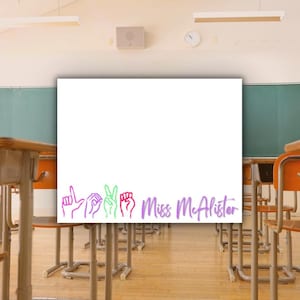 May include: White sign with the text "Miss McAlister" in purple script. Five colorful hand gestures are displayed below the text. The sign is in a classroom setting with desks and chairs.