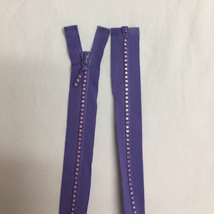 May include: A pair of purple zippers with iridescent rhinestones. The zippers are separated and ready to be sewn into a garment.