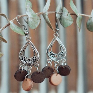 May include: Silver dangle earrings with a teardrop-shaped design and brown and beige wooden beads.