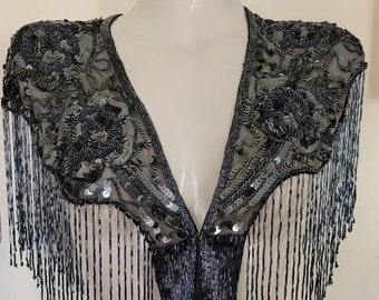 May include: A black bolero shrug featuring intricate beadwork and sequin embellishments in floral patterns. The garment is constructed from sheer mesh fabric and is finished with long, dangling beaded fringe along the edges.