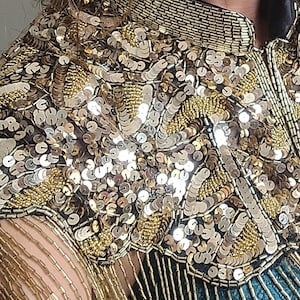 May include: A gold sequined top with a fringe trim. The sequins are arranged in a swirling pattern.