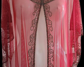 May include: A sheer, red cape-style garment with intricate beaded embellishments. The neckline and edges are adorned with detailed beadwork, and the fabric drapes elegantly. The garment is displayed on a mannequin against a black background.