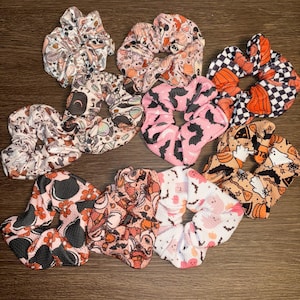 May include: A set of ten Halloween-themed scrunchies in various patterns. The scrunchies are made of soft, stretchy fabric and feature a variety of spooky designs, including pumpkins, bats, ghosts, and witches.