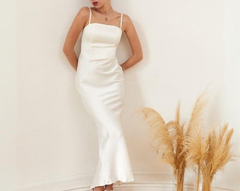 May include: A white satin dress with a fitted bodice and a flowing mermaid skirt. The dress has a simple, elegant design and is perfect for a special occasion.