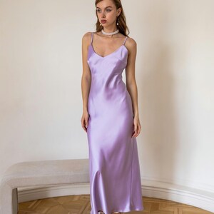 K&ouml;nnte beinhalten: Eine Frau tr&auml;gt ein lavendelfarbenes Satin-Slip-Kleid mit einer Perlenkette und wei&szlig;en Schuhen.