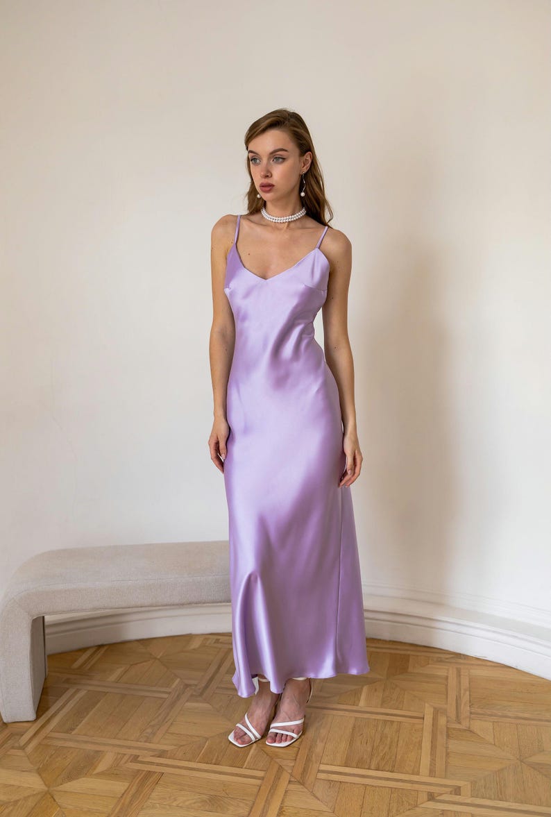 K&ouml;nnte beinhalten: Eine Frau tr&auml;gt ein lavendelfarbenes Satin-Slip-Kleid mit einer Perlenkette und wei&szlig;en Schuhen.