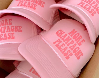 May include: A stack of pink trucker hats with the text "More Champagne Please" in pink letters.