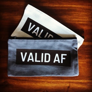 May include: Two gray and white canvas zippered pouches with the text "VALID AF" printed in white on a black background.