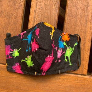 May include: A black face mask with a colorful frog pattern. The frogs are in various poses and colors, including pink, green, blue, and yellow.