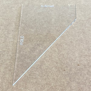 May include: A clear plastic template labeled "X-Small" with a diagonal line marked "FOLD". This template is used for sewing and crafting.