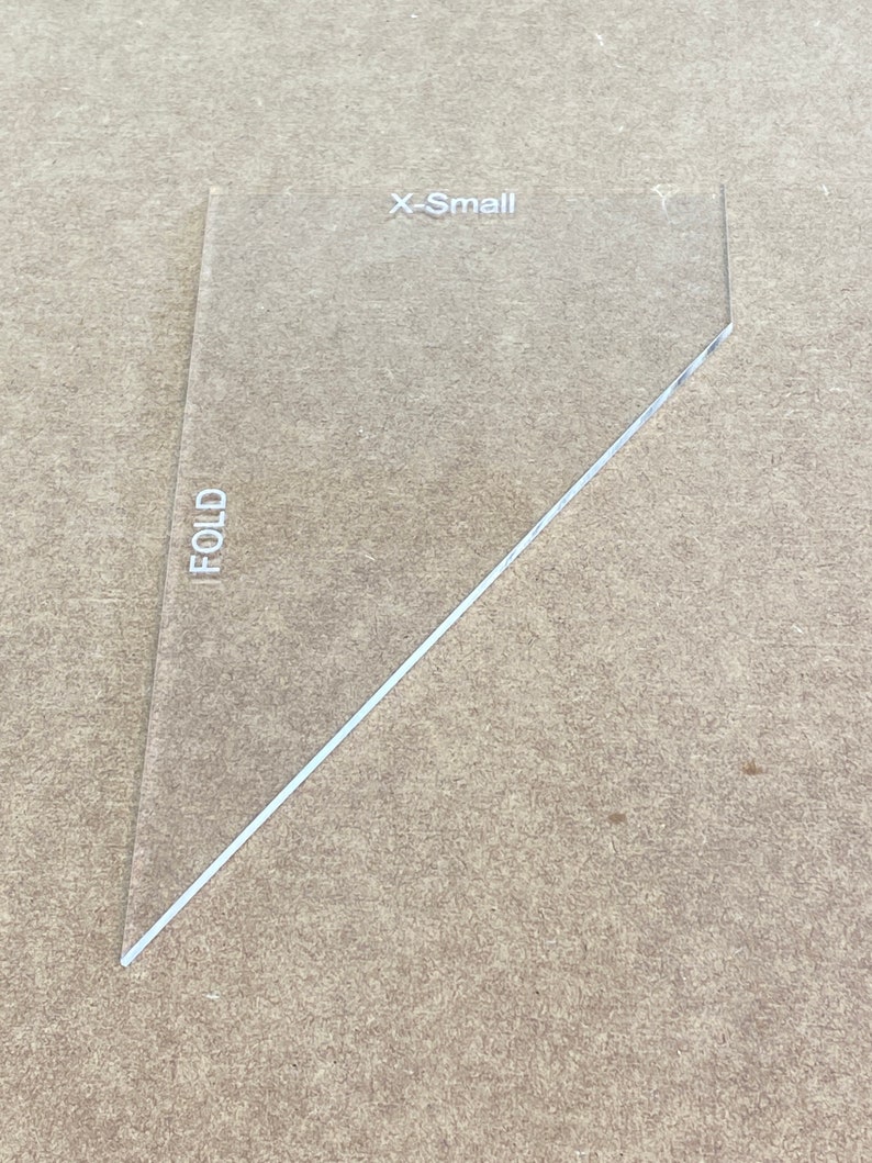 May include: A clear plastic template labeled "X-Small" with a diagonal line marked "FOLD". This template is used for sewing and crafting.