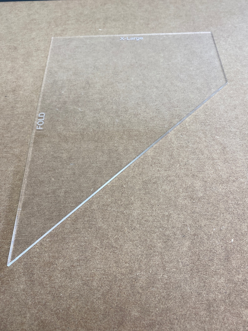 May include: A clear plastic triangle ruler with the word "FOLD" printed on the left side and "X-Large" printed on the top.