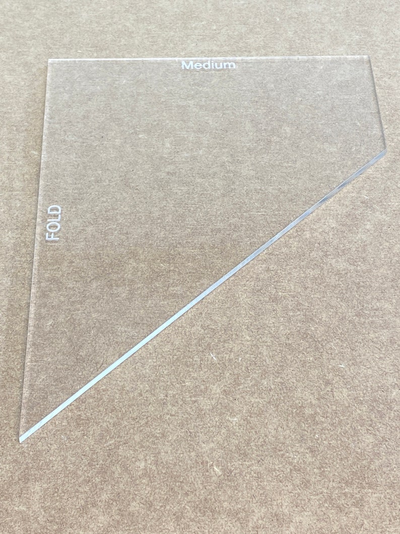 May include: A clear plastic triangle ruler with the word "Medium" printed on the top and the word "FOLD" printed on the left side.